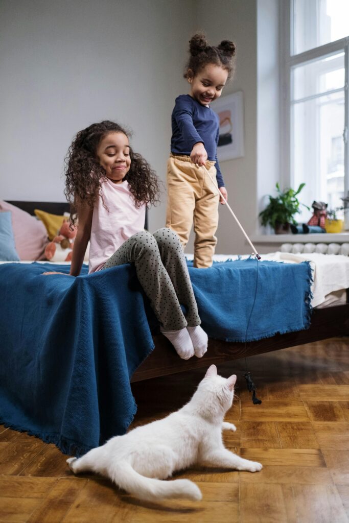 Two children playing with a cat indoors, enjoying playful bonding time.
